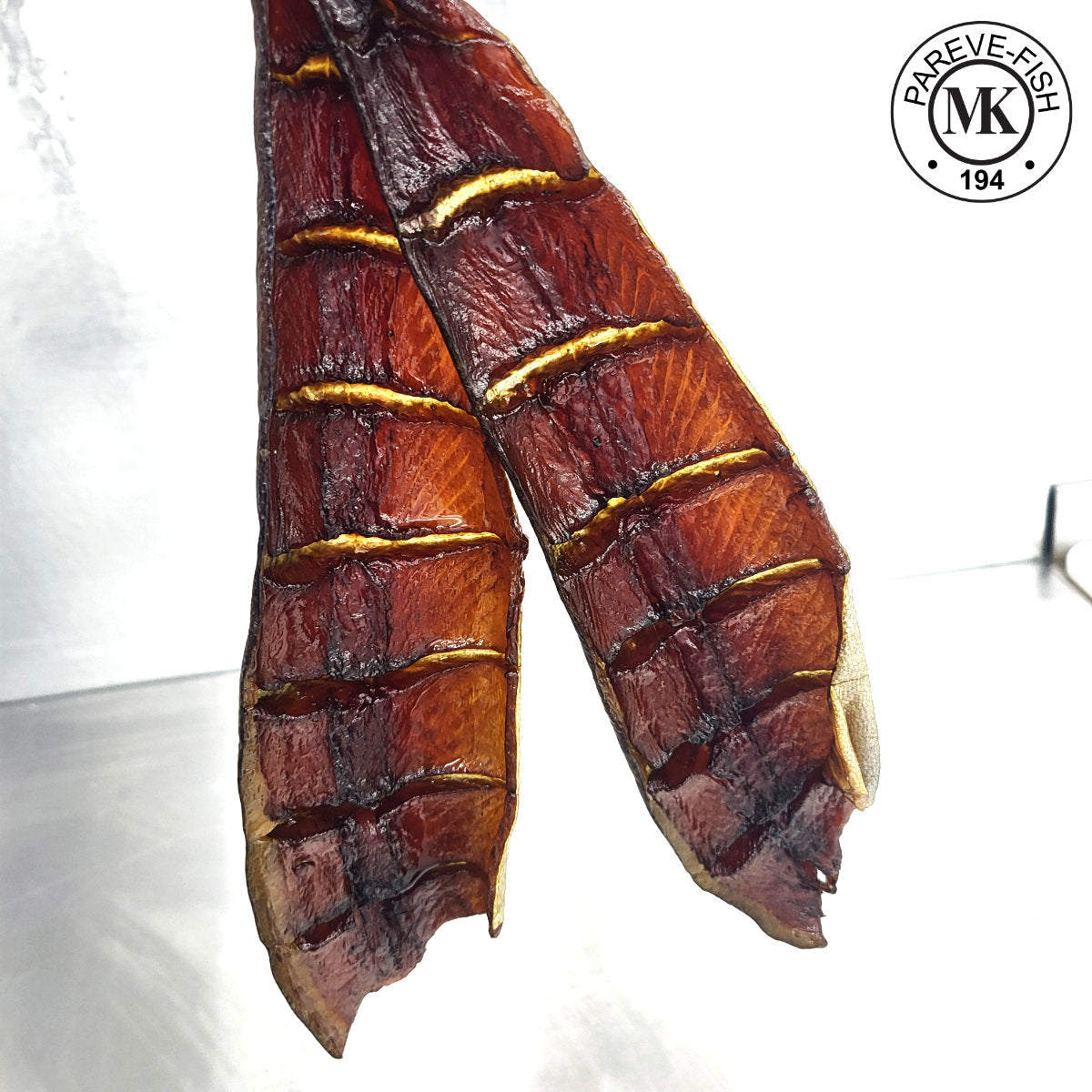Two dried candied rainbow trout yukola fillets with gold lines on a white background, featuring the MK logo.